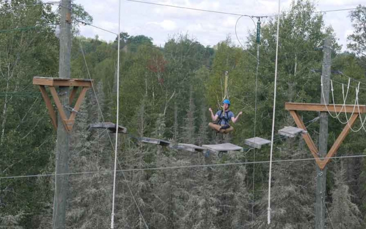 a student floats in a cross-legged position while being suspended in mid-air on a ropes course